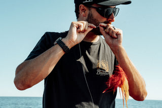 A fisherman tying a line using their teeth.