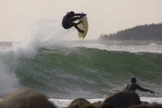 A surfer launching an air while his friend looks on.