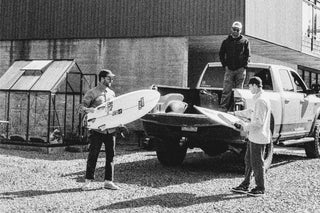 Three surfers loading boards into the back of a truck.