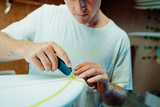 A surfboard shaper cutting tape with their utility knife.