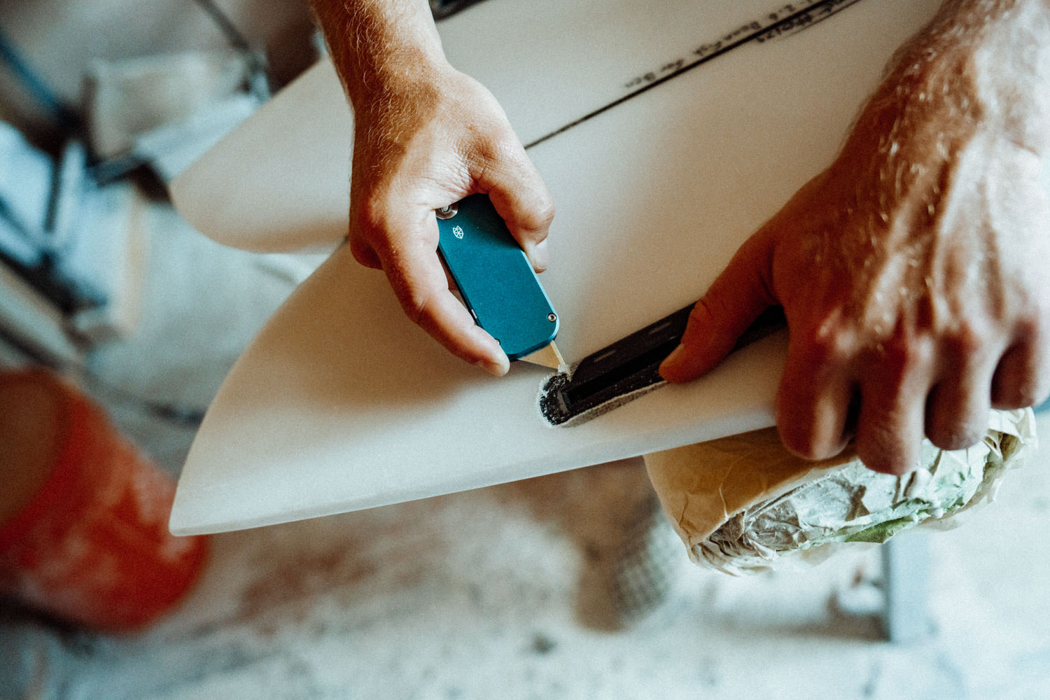 A person removing damaged foam from their surfboard with their Palmer utility knife.